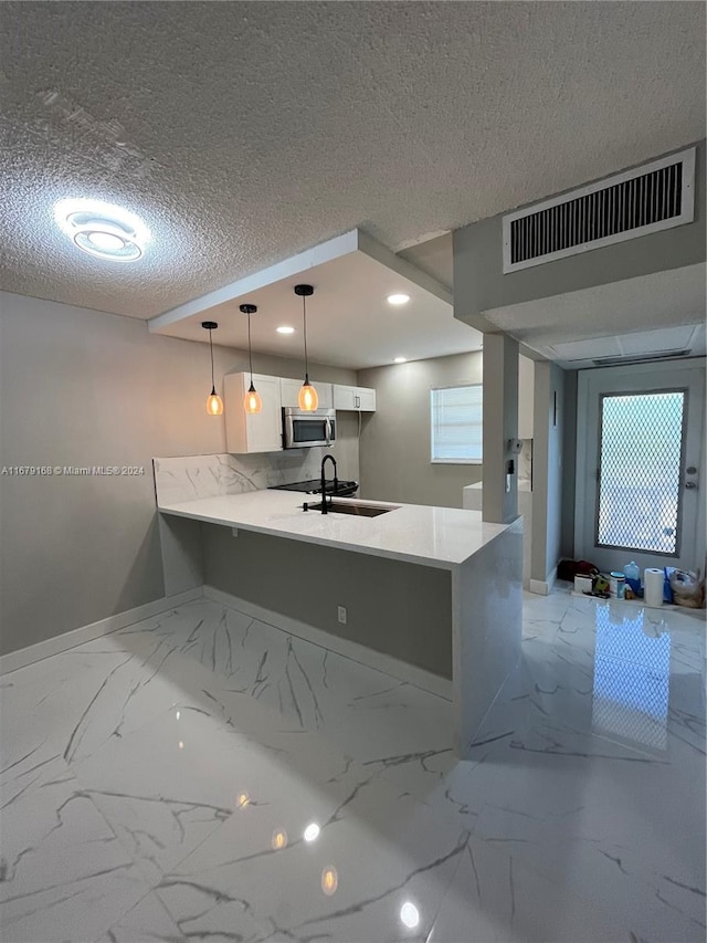 kitchen featuring sink, a textured ceiling, kitchen peninsula, white cabinetry, and decorative light fixtures