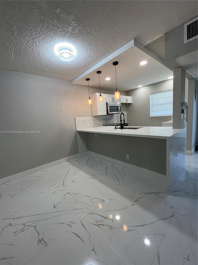 kitchen with kitchen peninsula, white cabinetry, a textured ceiling, sink, and decorative light fixtures