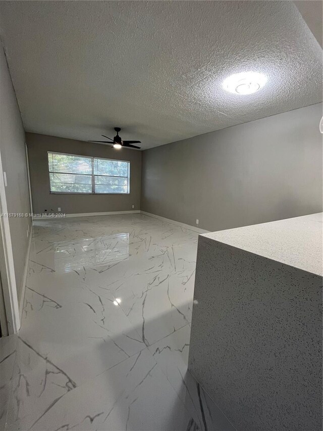 unfurnished room with baseboards, marble finish floor, a textured ceiling, and ceiling fan