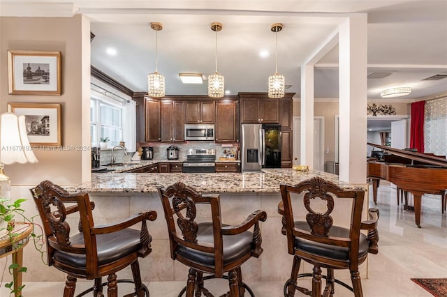 kitchen featuring kitchen peninsula, dark brown cabinets, decorative light fixtures, appliances with stainless steel finishes, and light stone counters