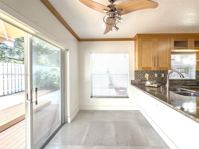 kitchen featuring ceiling fan, dark stone counters, ornamental molding, a textured ceiling, and sink