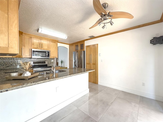 kitchen with sink, a textured ceiling, ornamental molding, dark stone counters, and appliances with stainless steel finishes