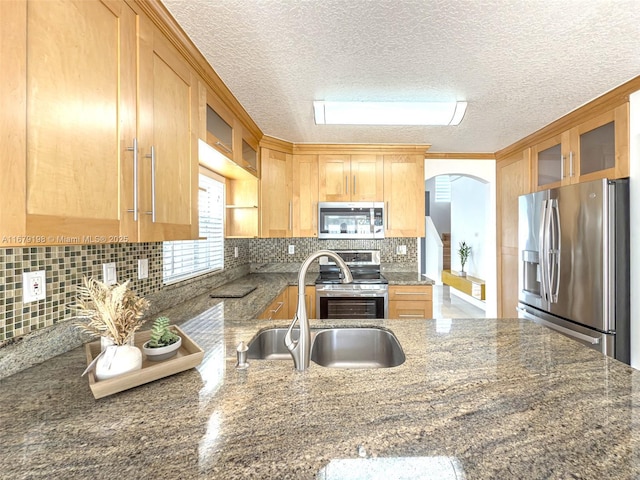 kitchen with stainless steel appliances, dark stone counters, a textured ceiling, sink, and tasteful backsplash