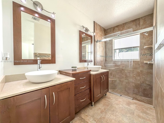 bathroom with a textured ceiling, tiled shower, and vanity