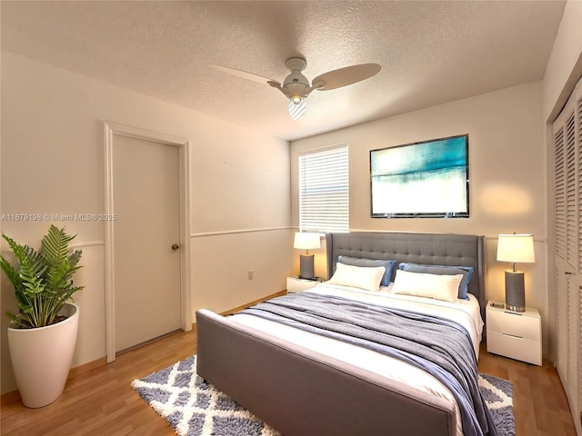 bedroom with light wood-type flooring, ceiling fan, a textured ceiling, and a closet