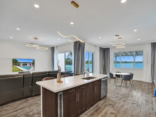 kitchen featuring hanging light fixtures, stainless steel dishwasher, light hardwood / wood-style flooring, sink, and a water view