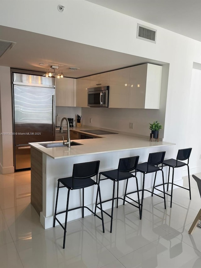 kitchen with sink, stainless steel appliances, kitchen peninsula, a breakfast bar area, and light tile patterned floors