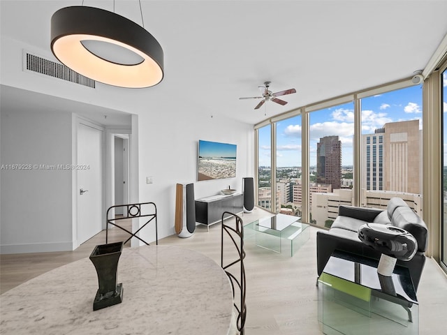 living room featuring ceiling fan, expansive windows, and light hardwood / wood-style flooring