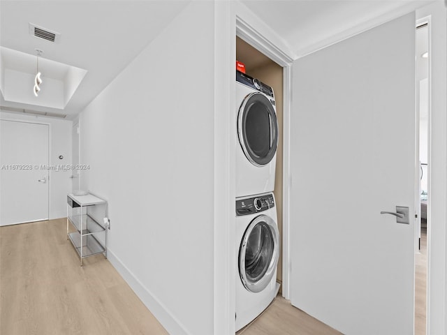 laundry room featuring stacked washer / dryer and light hardwood / wood-style flooring