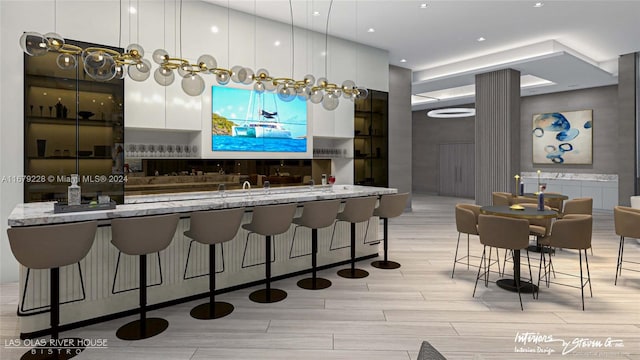 bar with light stone counters, light wood-type flooring, pendant lighting, and white cabinets