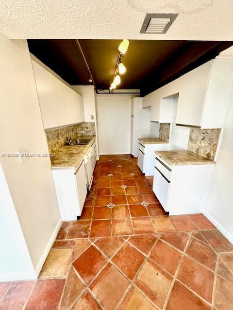 kitchen featuring tasteful backsplash, white cabinets, tile patterned floors, and sink