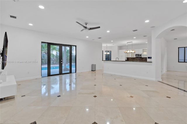 unfurnished living room featuring french doors and ceiling fan with notable chandelier