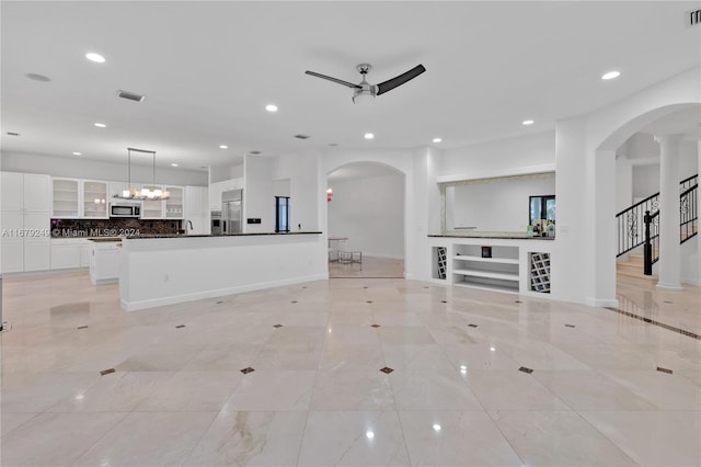 unfurnished living room featuring sink and ceiling fan with notable chandelier