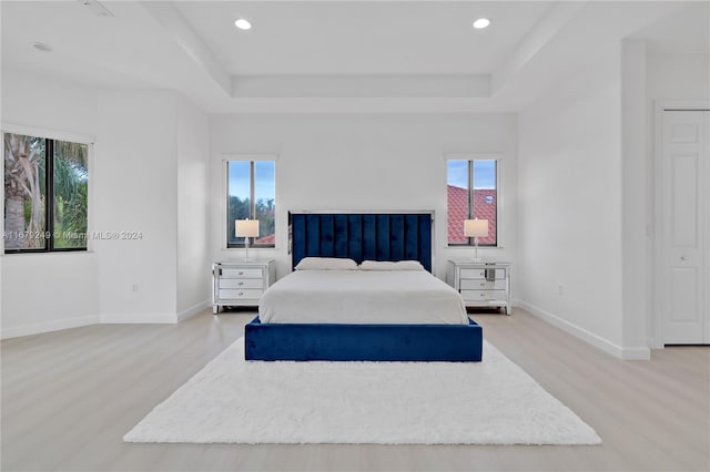 bedroom with light hardwood / wood-style floors, multiple windows, and a raised ceiling