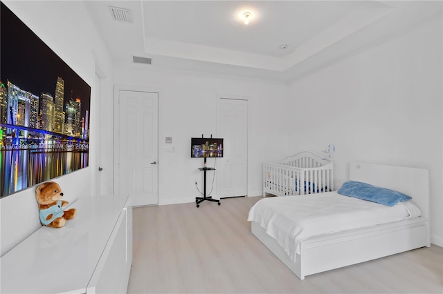 bedroom with a tray ceiling and light wood-type flooring