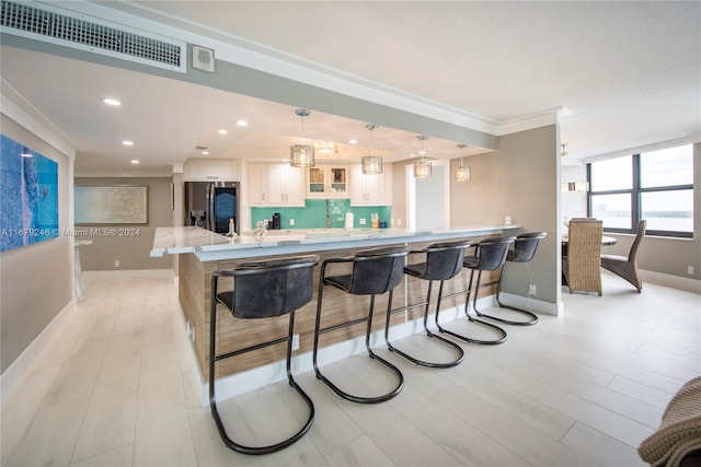 kitchen with stainless steel fridge, backsplash, a kitchen breakfast bar, ornamental molding, and pendant lighting