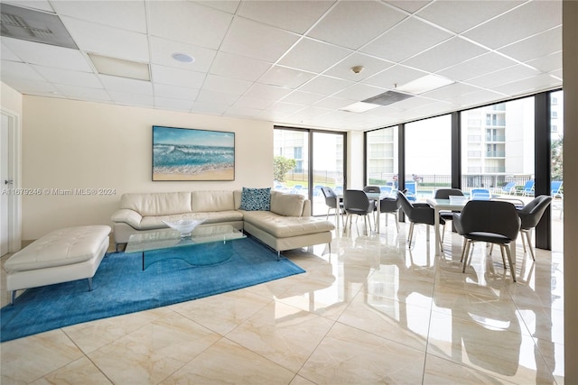 living room with a drop ceiling, a wall of windows, and light tile patterned floors