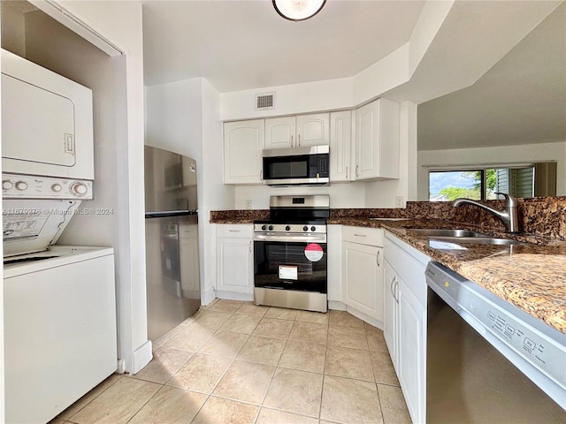 kitchen featuring white cabinetry, dark stone counters, stacked washer and dryer, sink, and stainless steel appliances