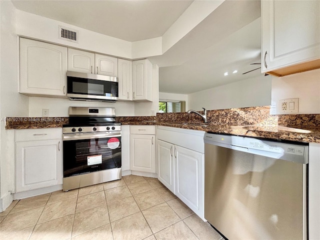 kitchen featuring dark stone countertops, sink, white cabinetry, light tile patterned floors, and appliances with stainless steel finishes