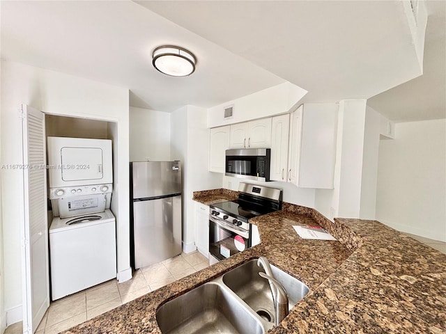 kitchen featuring appliances with stainless steel finishes, sink, stacked washer / dryer, white cabinets, and light tile patterned floors