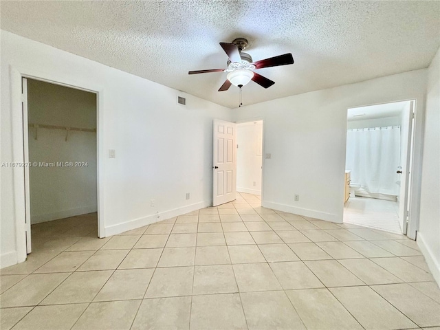 unfurnished bedroom featuring ensuite bathroom, a walk in closet, a textured ceiling, and ceiling fan