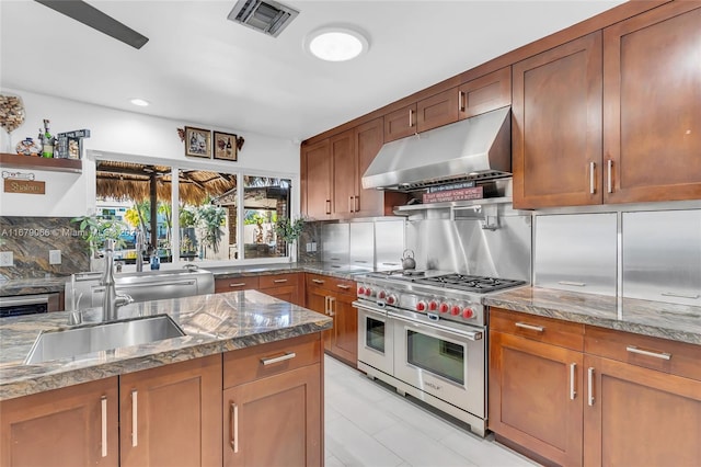 kitchen featuring light stone countertops, sink, range with two ovens, and backsplash