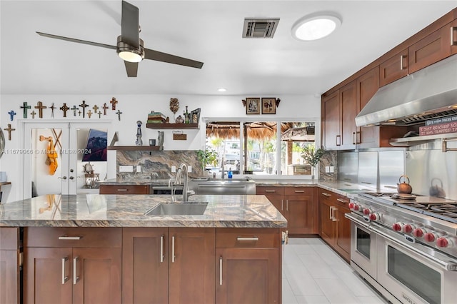 kitchen featuring light stone countertops, ventilation hood, an island with sink, and stainless steel appliances