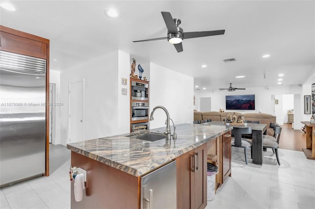 kitchen featuring a center island with sink, stainless steel built in fridge, sink, and stone countertops