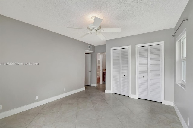 unfurnished bedroom featuring light tile patterned flooring, two closets, a textured ceiling, and ceiling fan