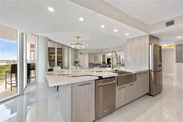 kitchen featuring light brown cabinets, sink, an inviting chandelier, appliances with stainless steel finishes, and light stone counters