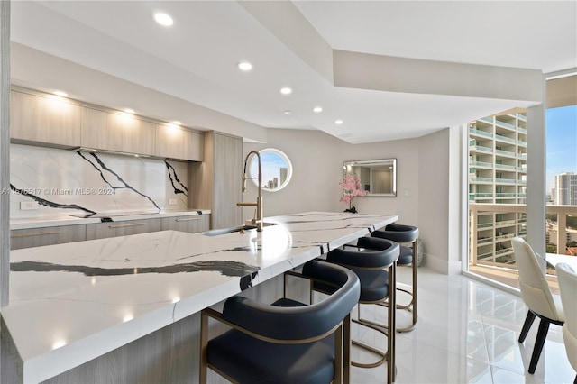 kitchen with an island with sink, a kitchen breakfast bar, light stone countertops, light brown cabinetry, and sink