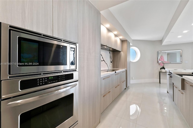 kitchen with sink, light stone countertops, light tile patterned floors, light brown cabinetry, and appliances with stainless steel finishes