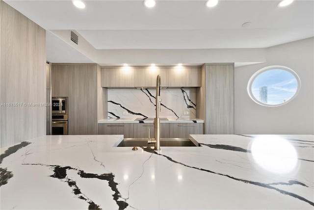 interior details with light stone counters, oven, and light brown cabinets