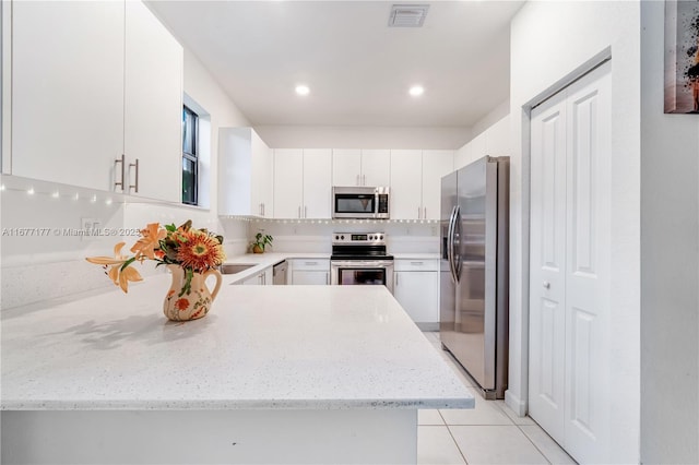 kitchen featuring visible vents, light stone counters, white cabinetry, stainless steel appliances, and a peninsula