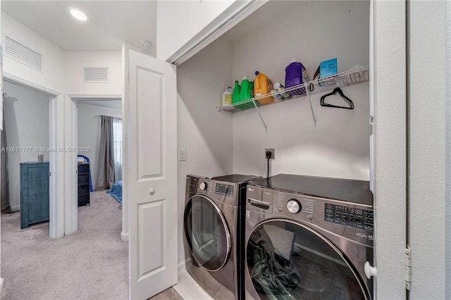 clothes washing area with laundry area, light colored carpet, visible vents, and washer and clothes dryer