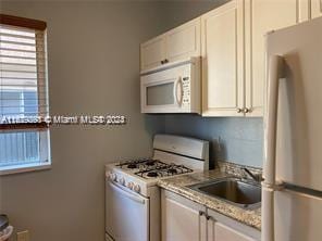 kitchen featuring white cabinets, light stone counters, white appliances, and sink