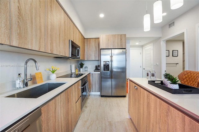 kitchen with appliances with stainless steel finishes, decorative light fixtures, sink, and light wood-type flooring