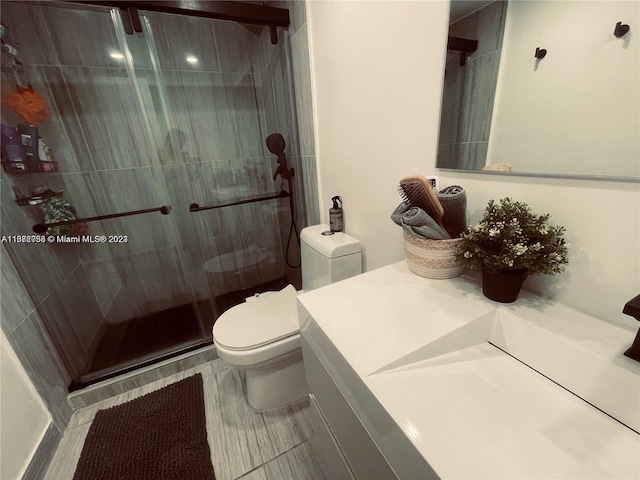 bathroom featuring a shower with door, toilet, and vanity