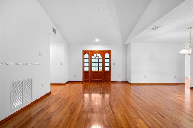 foyer with an inviting chandelier, vaulted ceiling, and light wood-type flooring