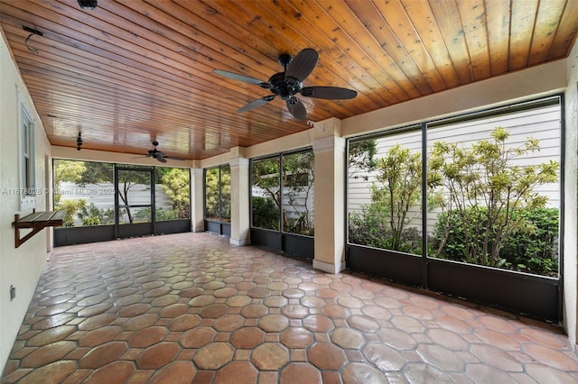 unfurnished sunroom featuring wood ceiling, ceiling fan, and a healthy amount of sunlight