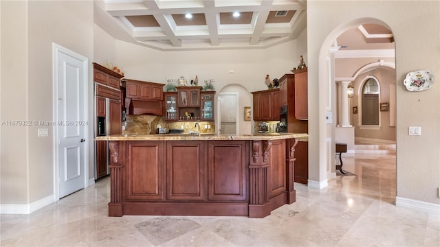 kitchen featuring tasteful backsplash, a towering ceiling, coffered ceiling, premium range hood, and a center island with sink