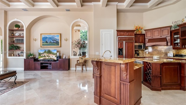 kitchen featuring beamed ceiling, paneled built in fridge, custom range hood, crown molding, and a center island with sink