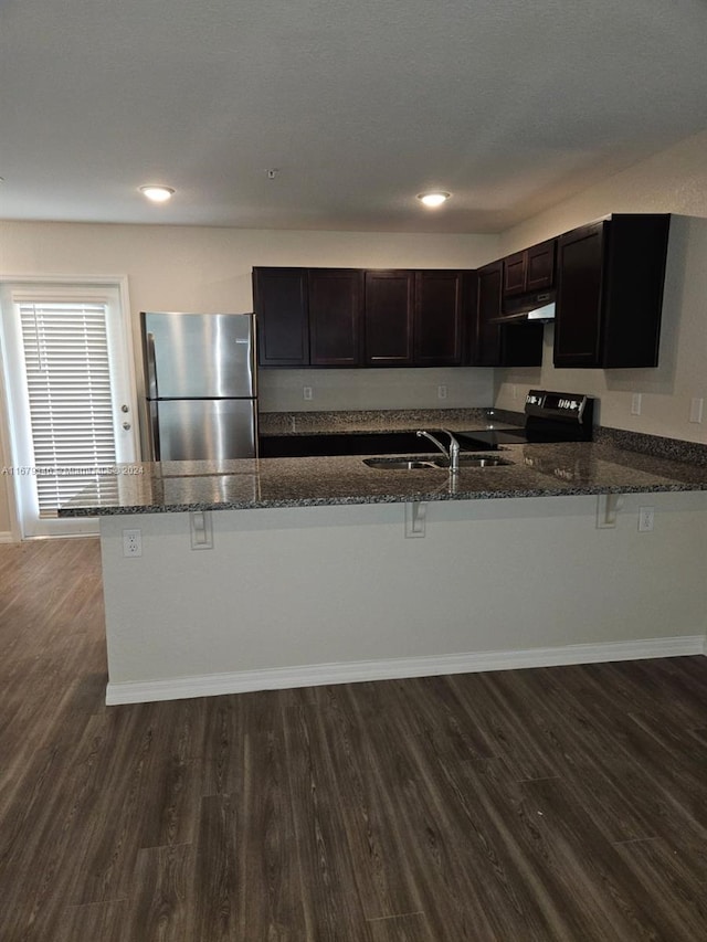 kitchen with dark hardwood / wood-style flooring, kitchen peninsula, dark stone counters, and stainless steel refrigerator