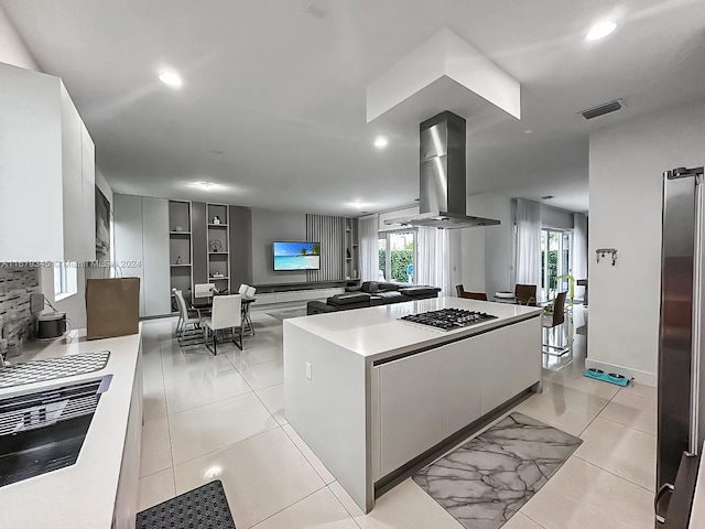 kitchen with a kitchen island, white cabinetry, stainless steel gas stovetop, light tile patterned floors, and exhaust hood