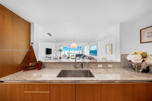 kitchen featuring light stone counters, sink, kitchen peninsula, and decorative light fixtures