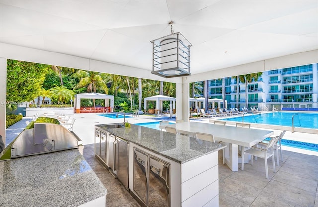 view of pool featuring a gazebo, grilling area, an outdoor wet bar, and a patio