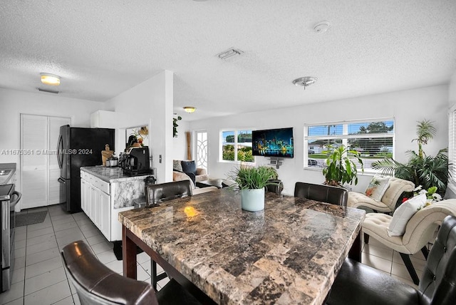 interior space with tile patterned floors, black fridge, stainless steel stove, white cabinets, and a textured ceiling