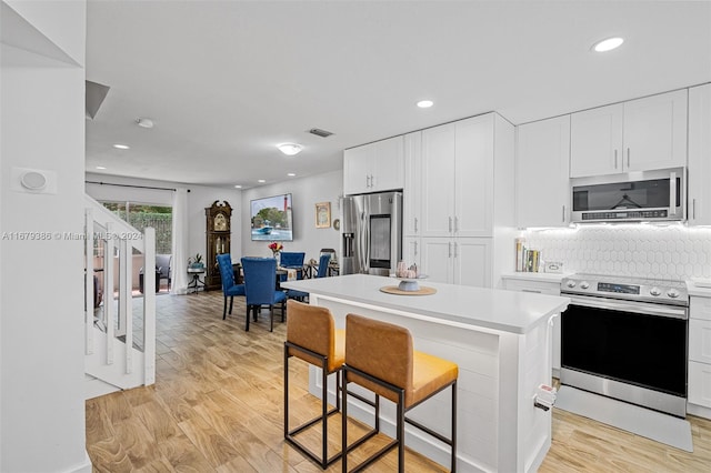 kitchen with a kitchen island, a kitchen breakfast bar, white cabinetry, stainless steel appliances, and light hardwood / wood-style flooring