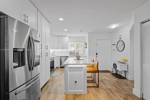 kitchen with a breakfast bar area, white cabinetry, light wood-type flooring, a kitchen island, and stainless steel appliances