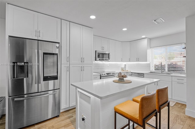 kitchen featuring sink, white cabinetry, appliances with stainless steel finishes, a kitchen breakfast bar, and a kitchen island